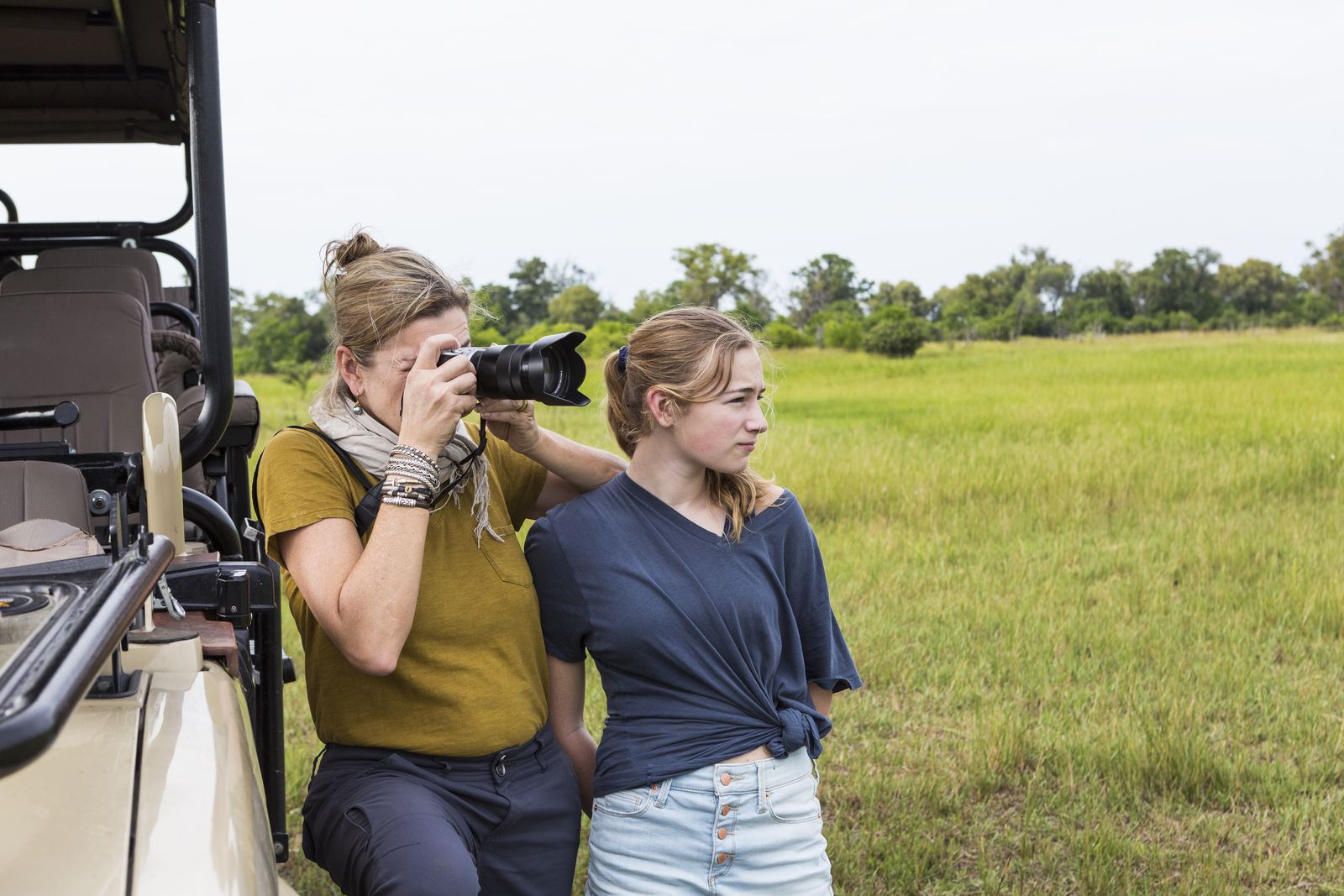 A mother and daughter photographing wildlife beside a safari vehicle
