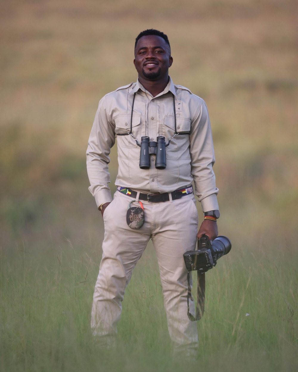 Brian Batsurana, professional safari guide, standing in golden grassland with binoculars and camera